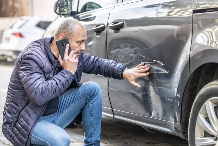 Mann sitzt neben beschädigtem Auto und beantragt einen Sofortkredit